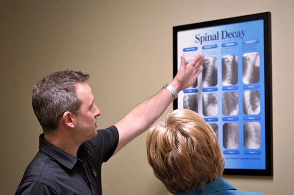 Dr. Eric Mayfield examining a "Spinal Decay" poster showing stages of spinal degenerationwith a patient,
